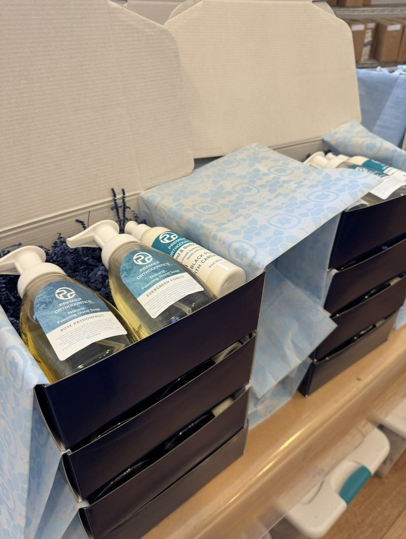 Stacks of navy gift boxes lined with blue tissue being packed with custom-labeled foaming hand soap and lotion