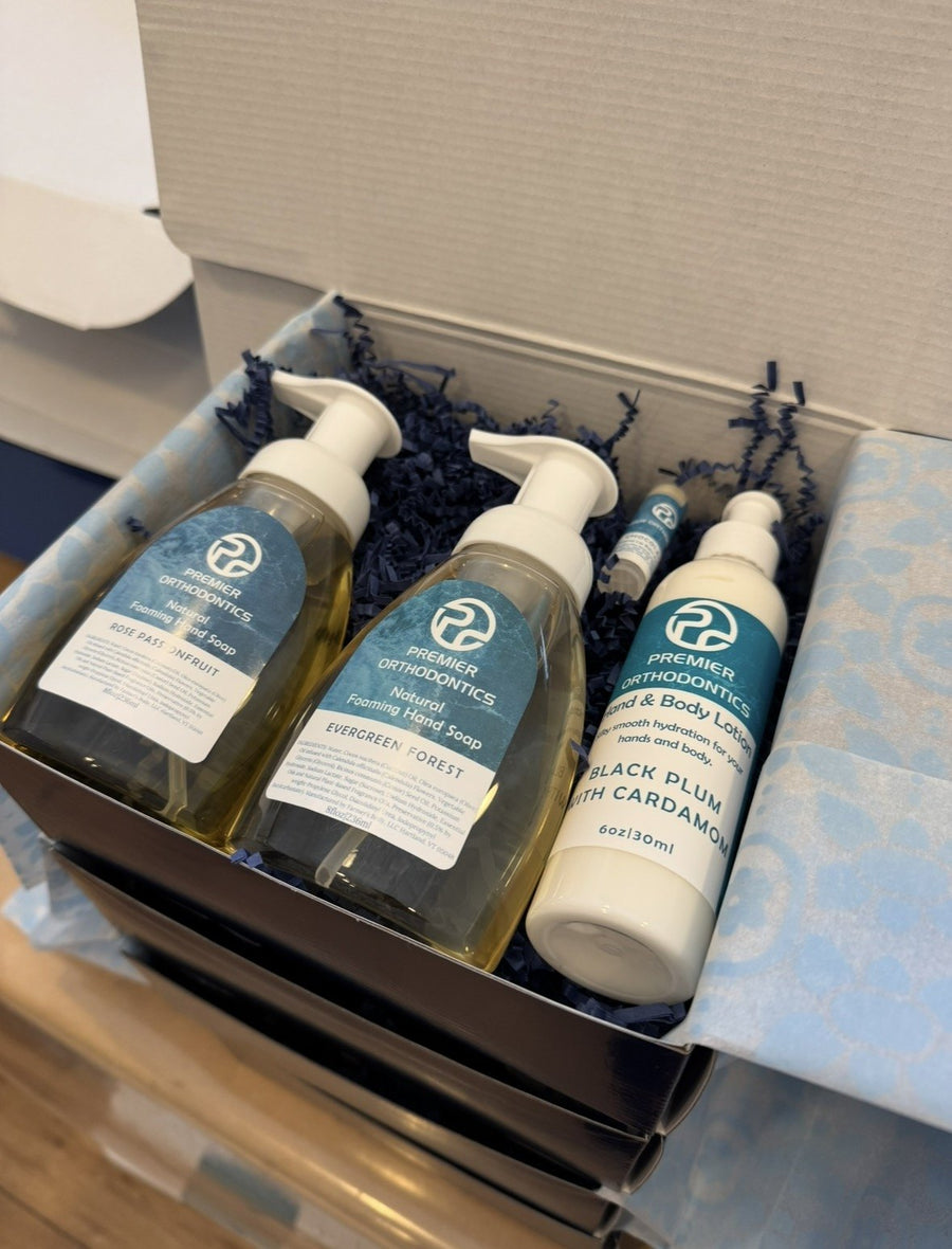 A mailer box lined with blue tissue, packed with an orthodontic practice's custom-labeled foaming hand soaps, hand and body lotion, and lip balm