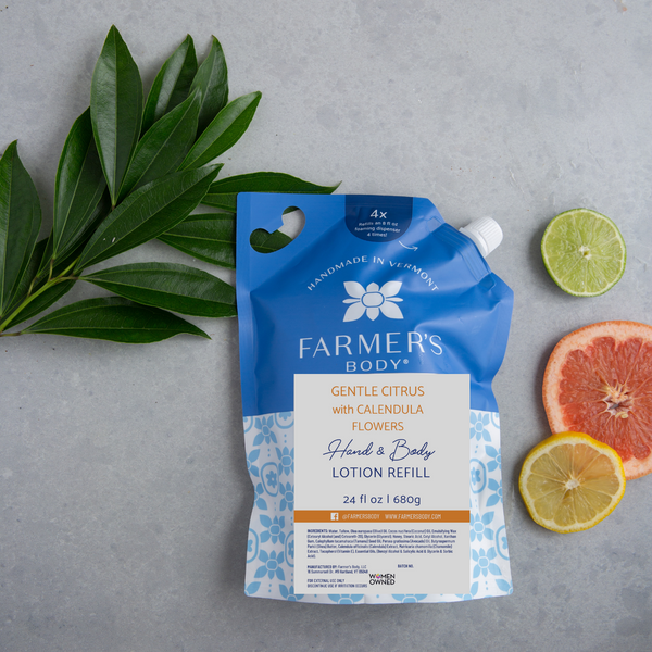 A pouch of Farmer's Body hand and body lotion refill, with a blue label, placed next to citrus fruits and green leaves on a grey background.